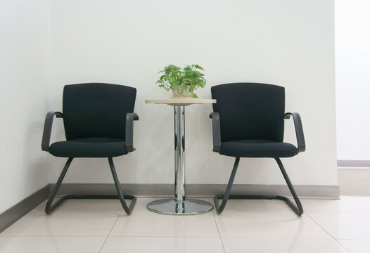 Two black office chairs in a corridor or waiting area, table with a small green plant.