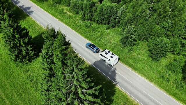 Aerial view of a blue car traveling alongside a white camper on a winding rural road