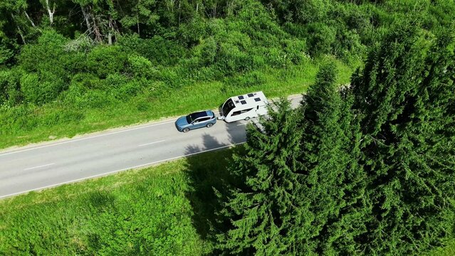 Aerial view of a car towing a caravan along a winding road surrounded by lush greenery