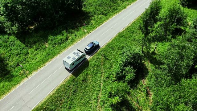 Camper van being towed by SUV on a rural road surrounded by lush green vegetation