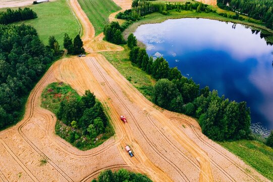 Tractors navigating earthy paths beside a serene pond surrounded by lush trees in Finland