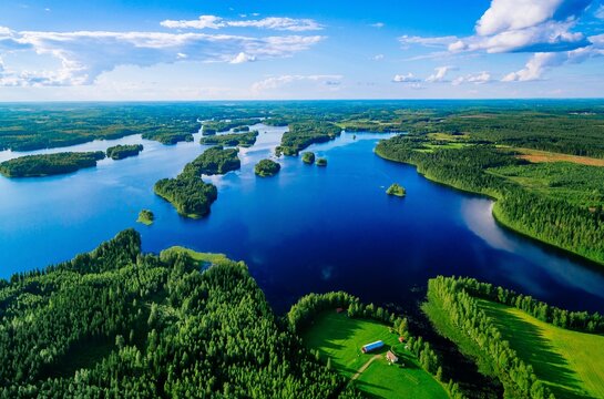 Aerial view of lush green forests surrounding tranquil blue lakes under bright blue sky in Finland