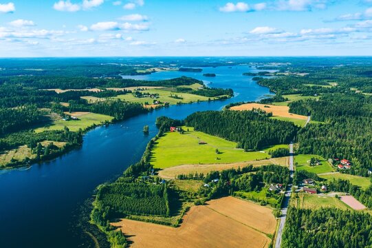 Aerial view of lush green fields bordered by a winding river and scattered farmhouses in summer in Finland