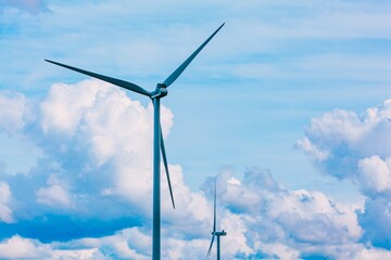 Wind turbine blades spinning against a cloudy blue sky with white clouds at sunset in Finland © NBLX