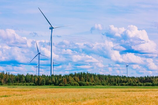 Three towering wind turbines rotating against a backdrop of fluffy clouds and green forest in Finland