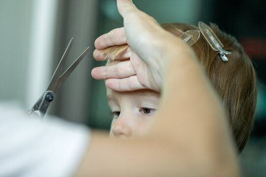Mother trimming boy hair with scissors seen from behind view at home