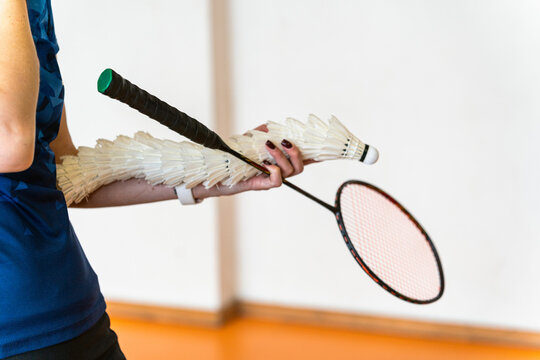 badminton coach holding feather shuttlecock stack and racket indoors