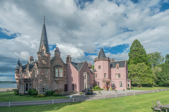 A large historic gothic style country house, a tall spire and pointed roofs.