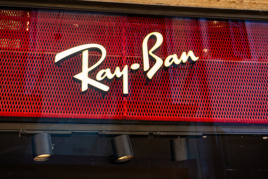 Ray Ban Logo Sign on a Red Metal Mesh Background with Spotlights at Store Entrance Exterior. Verona, Italy - June 25, 2026