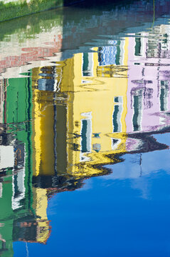 Reflections of yellow and green house fronts in the water of the canal at Burano.