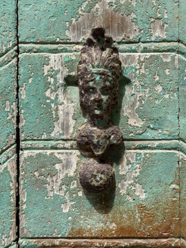 Weathered Door Knocker, a decorative figure of a person with a shell headdress in Chianalea