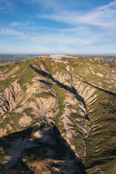 Hilltop town of Pisticci with white buildings, and the deep fissures of the Calanchi landscape below, eroded clay ridges.