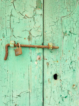 Weathered Door with a metal bolt and padlock, green peeling paint, in the town of Pisticci