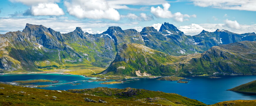 Nordland, Norway - 12.07.2020: Panoramic view of jagged green mountains and turquoise fjords under a bright summer sky