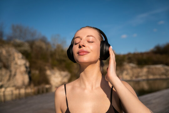 Portrait of female model relaxing after workout with playlist. Young woman embracing healthy lifestyle beneath blue sky. Active wellness concept.
