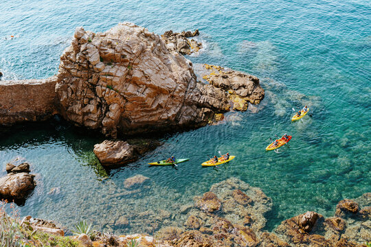 Group of kayaks on clear blue water near rocky coastline in Blanes, Costa Brava, Spain