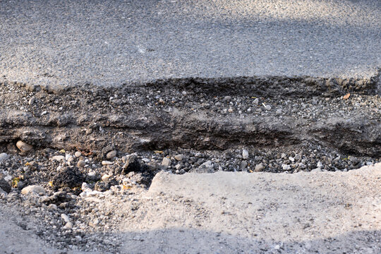 Damaged asphalt road with a deep pothole and broken pavement surface. Road deterioration highlights concepts of infrastructure maintenance, transportation, and public safety.