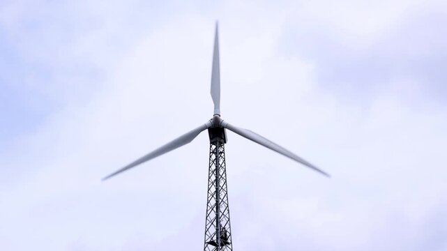 A towering wind turbine slowly rotates against a soft, overcast sky, symbolising clean energy and sustainable power. Captured in ultra-high-definition 4K