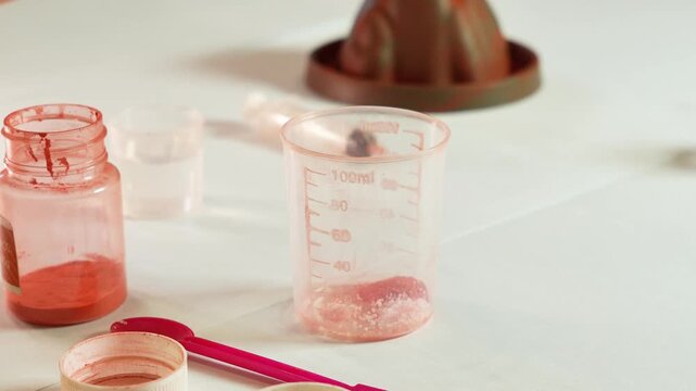 A child pours chemical reagents into measuring cups. Children's chemical experiment Volcano. Effervescent reaction of soda and citric acid and water. Children's toy, experiment, learning, orange, red.