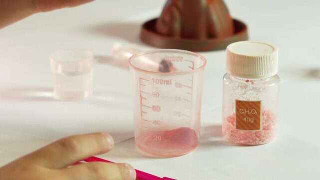 A child pours chemical reagents into measuring cups. Children's chemical experiment Volcano. Effervescent reaction of soda and citric acid and water. Children's toy, experiment, learning, orange, red.