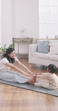 Asian mother and cute daughter doing stretch yoga pose together on a mat at home.