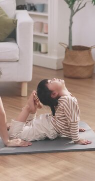 Flexible Asian cute little girl performing cobra stretch yoga pose touching feet to her head at home.