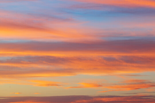 The sky at sunrise above the Chaggaga Sand Dunes, light clouds reflecting red and orange light against blue sky.