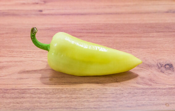A single Hungarian white wax pepper, also known as TV paprika or t&ouml;lteni val&oacute;, lying on a wooden table.