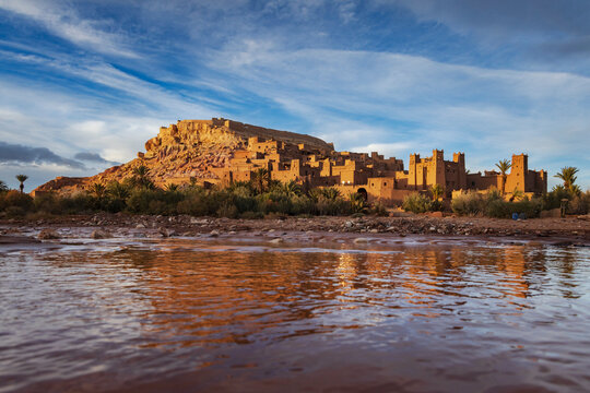 The Ksar of Ait Ben Haddou buildings reflected in Oed El Maled lake water at sunset.