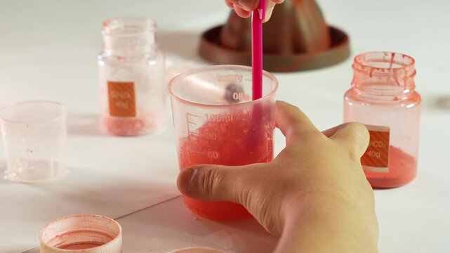 Child stirs chemical reagents. Children's chemical experiment Volcano. Effervescent reaction of soda and citric acid and water. Children's toy, experiment, learning, orange, red.