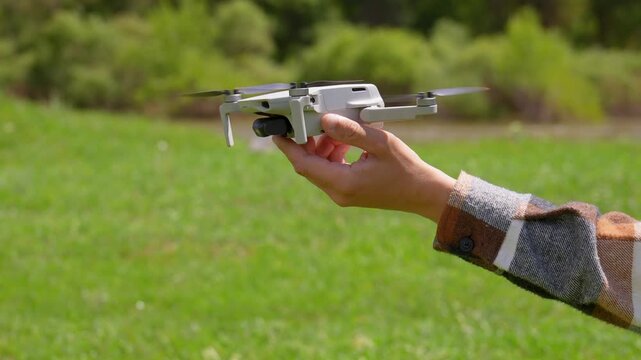 Close-up of the hands of a man launching a small modern quadcopter from his hand on a grass field. The pilot's hand releases the UAV, which then hovers and flies away over the green landscape