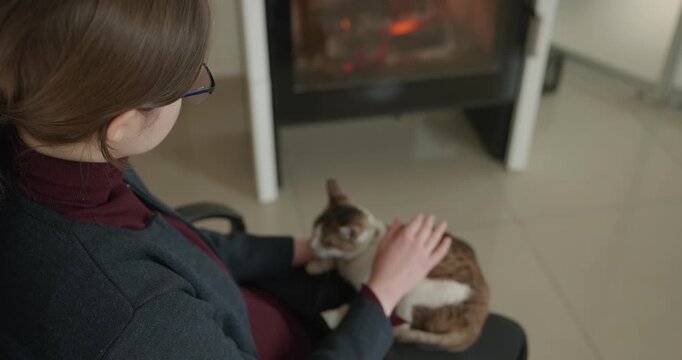 Girl Hold Kitten Tabby Cat on Laps Relaxing Near Fireplace at Home. 4K 10-bit