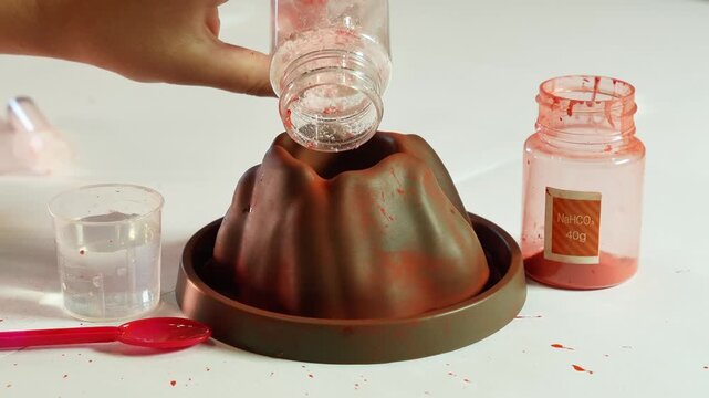 A child pours chemical reagents into a plastic Volcano. Children's chemical experiment Volcano. Effervescent reaction of soda and citric acid and water. Children's toy, experiment, learning, orange,