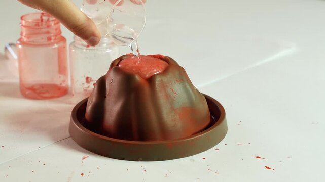 Child adds water to chemical reagents. Children's chemical experiment Volcano. Effervescent reaction of soda and citric acid and water. Children's toy, experiment, learning, orange, red.
