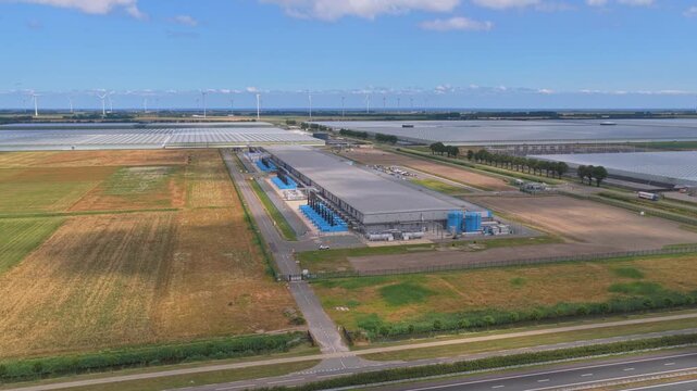 Aerial view of the google data center in middenmeer, netherlands. The facility is surrounded by farmland, greenhouses, and wind turbines