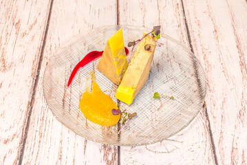 Overhead close-up of foie gras wedges with mango puree, berry sauce, and delicate microgreens on textured glass. © Toyakisfoto.photos