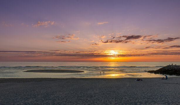 Golden sunset over Costa Nova Beach near Aveiro, Portugal. Warm sunlight reflecting on the calm Atlantic Ocean creates a peaceful coastal landscape with dramatic clouds .