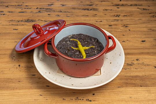 Simmered Black Beans Topped with Chili Pepper in a Small Red Pot on Rustic Table