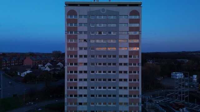 Slow drone reveal of a high-rise flat at dusk, construction surrounds base.