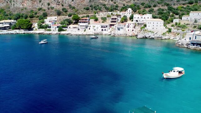 Drone footage of traditional fishing boats floating in the crystal-clear turquoise waters of Limeni Bay, Mani, Greece, with historic stone buildings along the Mediterranean coastline.