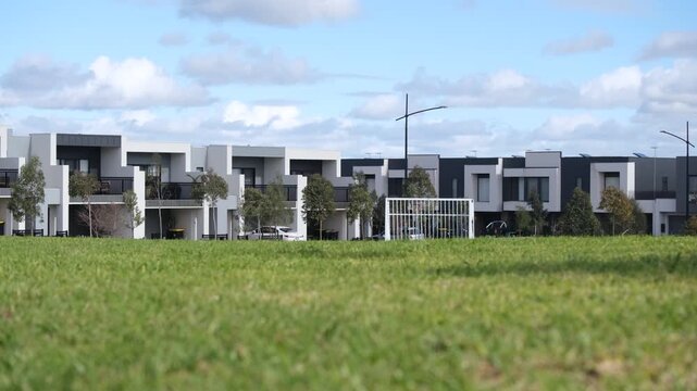 Modern two-storey townhouses facing a grassy public parkland with a soccer goal. Concept of community sports grounds, local infrastructure, and recreation facilities