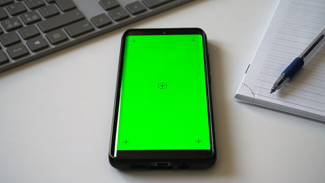 Smartphone with green screen chromakey on white desk.