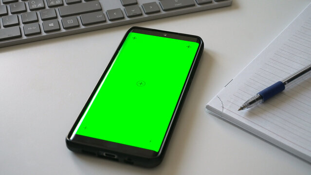 Smartphone with green screen chromakey on white desk.