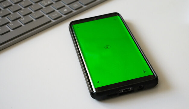 Smartphone with green screen chromakey on white desk.
