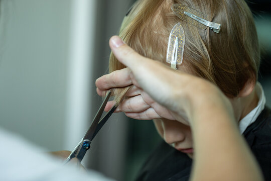 Mother cutting hair of young boy at home using scissors while holding section of hair