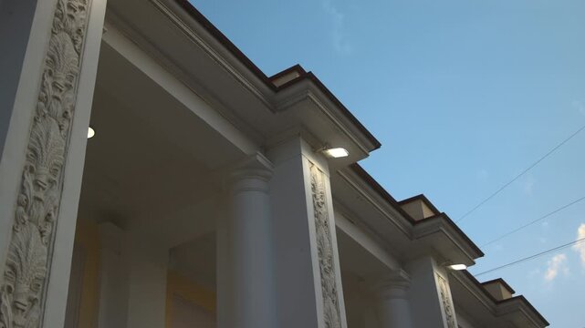 Low viewpoint of classical building facade corner with illuminated cornice, repeating columns and ornate pilasters beneath blue evening sky and warm exterior lamps