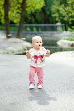 A young child walks carefully on a path in a park. Trees and a small body of water are nearby. The child looks happy while trying to balance on their feet.