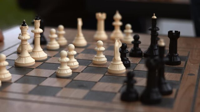 Low angle chessboard scene with white pieces advancing across squares while hands hover near board edges in focused game setting, with chess, board, piece, pawn detail