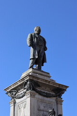 Fototapeta premium A bronze statue of Camillo Cavour stands atop an ornate stone pedestal against a clear blue sky.