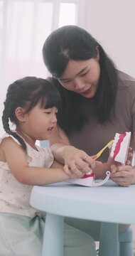 Asian mother teaching her little daughter how to brush teeth using a tooth model at home.